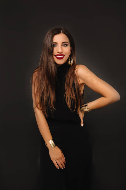 Stylish woman wearing black suit with long dark hair and bright make up posing over black background  - Foto, Imagem