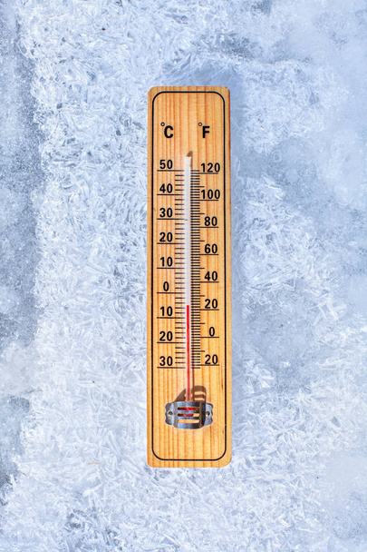 Thermometer laying on ice, showing minus 5 degrees. Sun shining  - Photo, Image