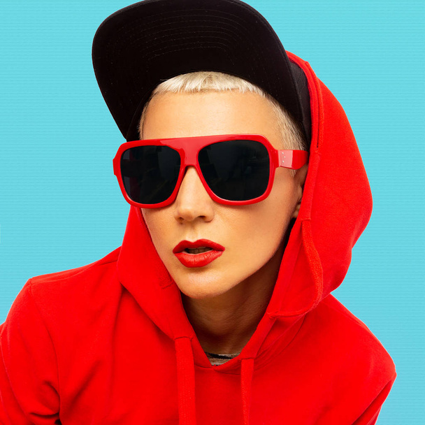 Fashion tomboy girl in red sweatshirt hoodie and sunglasses stre - Foto, afbeelding