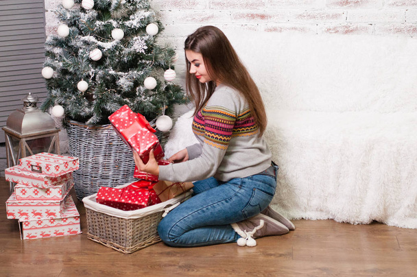 Stílusos csinos szexi nő a farmer és pulóver ül, közel a karácsonyfát, és úgy véli, ajándékok - Fotó, kép