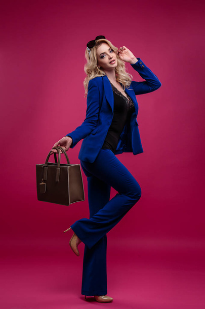 Pretty young blonde woman in a stylish fashionable costume holding handbag over pink background isolated - Φωτογραφία, εικόνα