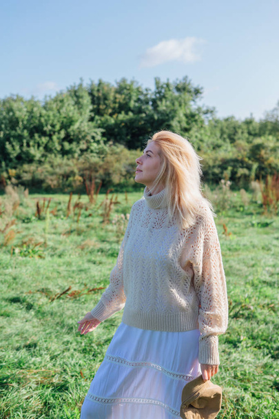 Beautiful blond woman staying and smocking cigarette in a green field - 写真・画像
