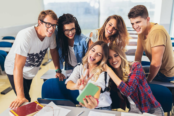 Χαρούμενοι μαθητές κάνουν ομαδική selfie στο smartphone στην τάξη. - Φωτογραφία, εικόνα