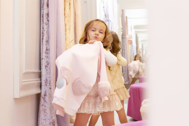shopping. discounts. little girl shopaholic. girl trying on a beautiful dress gently pink in the fitting room of the boutique. shopping center, shopping. emotions - Foto, imagen