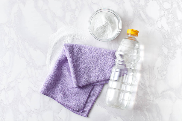 Vinegar in a bottle, baking soda and a cleaning cloth on a marble surface - Foto, Imagen