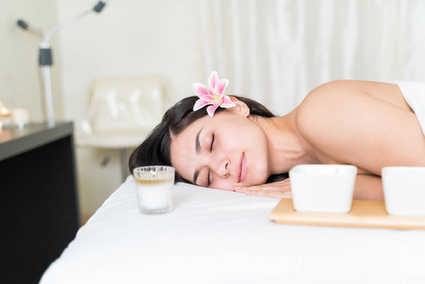 Relajada joven hermosa mujer hispana durmiendo en la cama con flor sobre oreja en spa de belleza
 - Foto, imagen