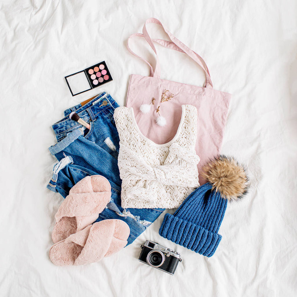 White knitted sweater, blue jeans, eco bag and hat on bed on white sheet. Women's stylish autumn or winter outfit. Trendy  clothes collage. Flat lay, top view.  - Fotografie, Obrázek