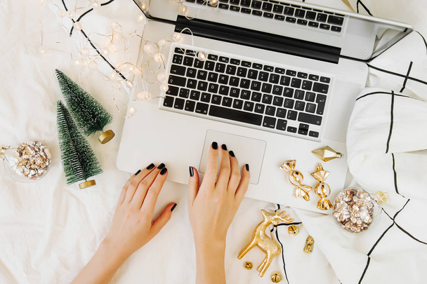 Christmas online shopping.  Woman buys presents online. Laptop with Christmas decorations on white bed with a blanket. Holiday concept. Flat lay, top view   - Zdjęcie, obraz