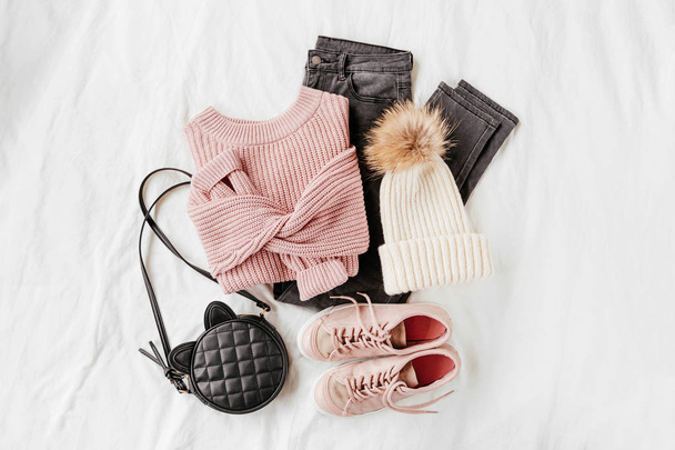 Pale pink warm sweater and gray trousers with sneakers, handbag on white sheet. Women's stylish autumn or winter outfit. Trendy clothes collage. Flat lay, top view.  - Fotografie, Obrázek
