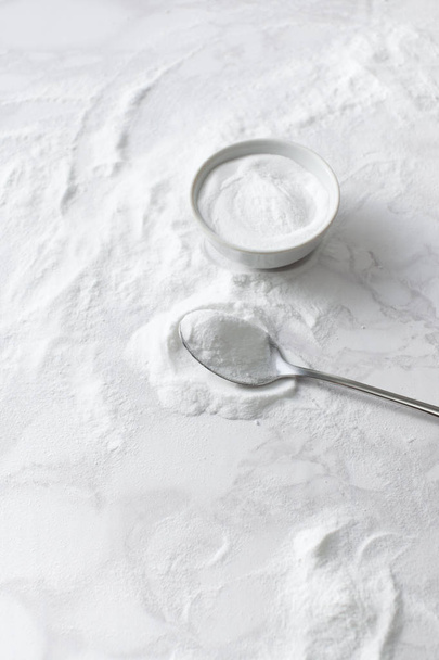 Baking soda in a bowl and in a spoon on the marble countertop - Zdjęcie, obraz