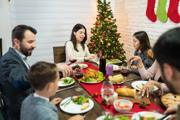 Noel partisinde yemek masasında ailesine yemek servisi yapan gülümseyen kadın. - Fotoğraf, Görsel