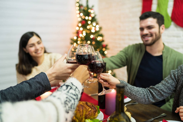 クリスマスパーティーのダイニングテーブルでワイングラスをクリックする友人の作物のイメージ - 写真・画像