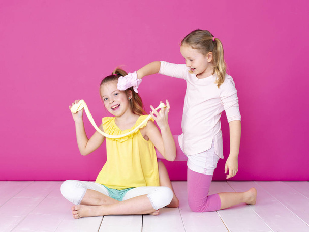 sisters having fun while playing with homemade slimes in front of pink background  - Foto, afbeelding