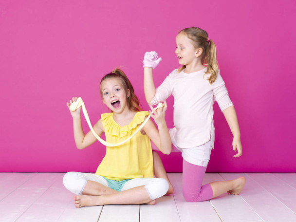 sisters having fun while playing with homemade slimes in front of pink background  - Fotoğraf, Görsel