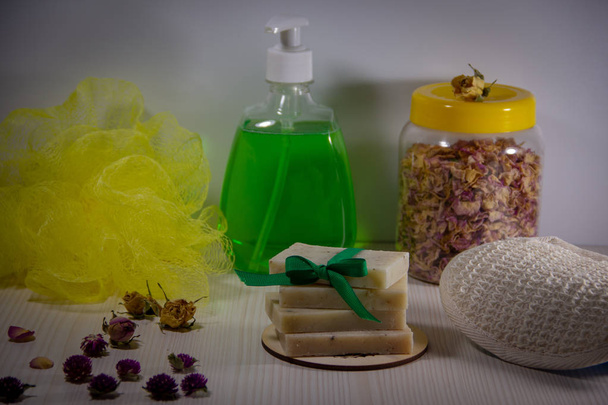 弓で飾られた手作りの天然石鹸、瓶にバラの花びらを乾燥させ、ボトルに液体石鹸、体のための2つの洗濯機。バスアクセサリー. - 写真・画像