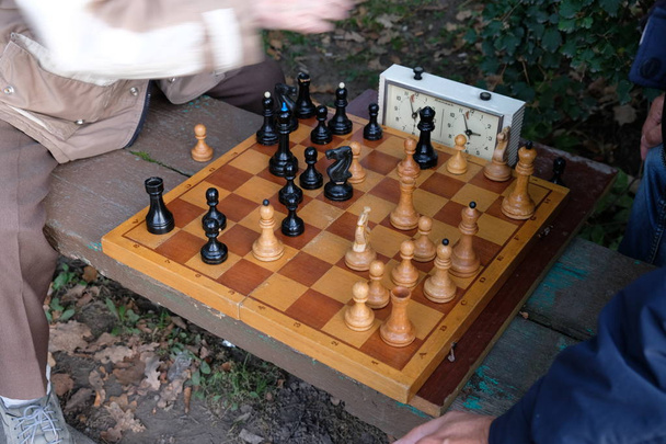 Двоє чоловіків грають у шахи. Дерев'яні шахові фігури на дерев'яній дошці. Початок вечірки, дебют. Гра відбувається проти годинника. Паркова лавка. Осінній день
. - Фото, зображення