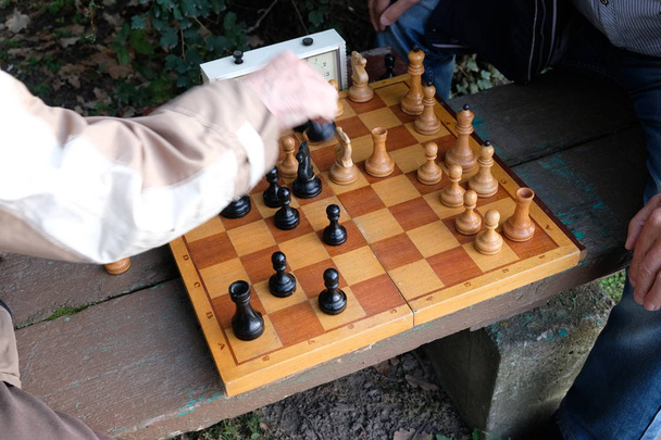 Двоє чоловіків грають у шахи. Дерев'яні шахові фігури на дерев'яній дошці. Початок вечірки, дебют. Гра відбувається проти годинника. Паркова лавка. Осінній день
. - Фото, зображення