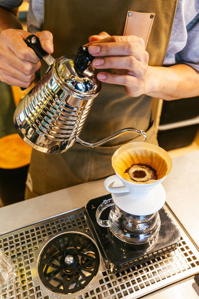 Ο μπάρμαν φτιάχνει καφέ με εναλλακτική μέθοδο που ονομάζεται στάζει. Μύλος καφέ, περίπτερο καφέ και χύνουμε σε ένα ξύλινο τραπέζι. - Φωτογραφία, εικόνα