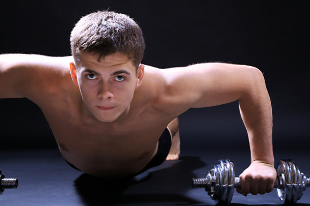 Handsome young muscular sportsman execute exercise with dumbbells on dark background - Fotoğraf, Görsel