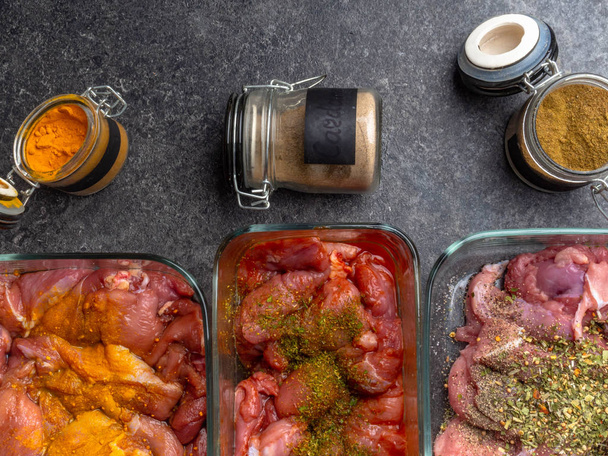 verschillende soorten vlees gebeeld in glazen kommen, potten met specerijen AD kruiden als curcuma, cardamon, rozemarijn op grijze achtergrond - Foto, afbeelding