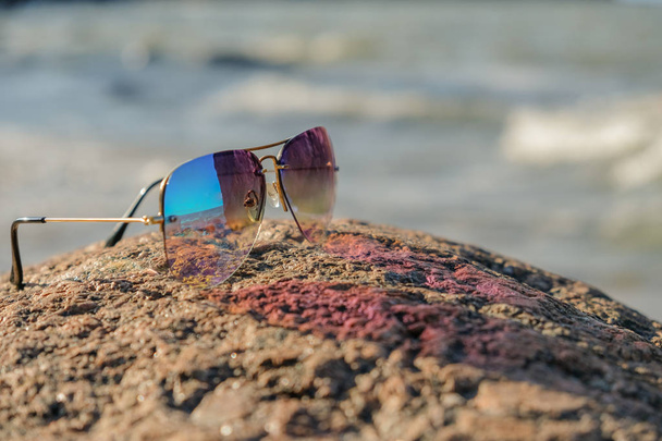 Odbicie krajobrazu w okularach. Kolorowe okulary leżą na granitowym kamieniu. Jesień, słoneczny dzień. Brzeg morza. - Zdjęcie, obraz