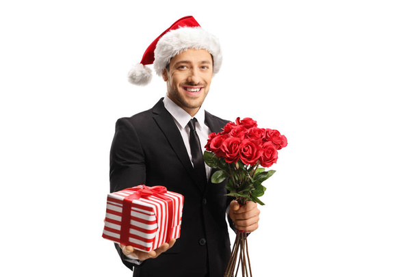 Young elegant man wearing a suit and a Santa hat holding roses a - Valokuva, kuva
