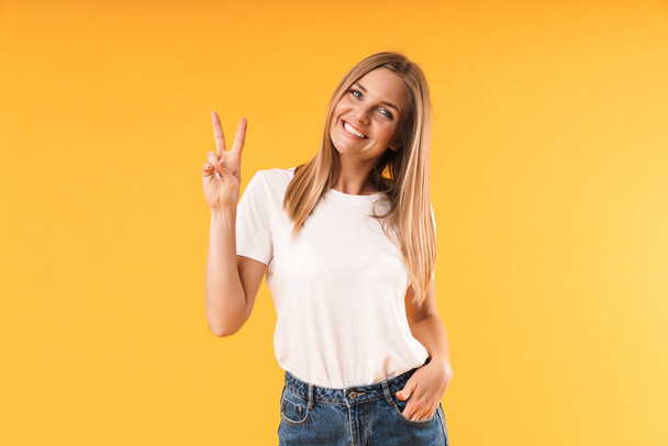 Image of attractive blond woman wearing casual t-shirt smiling at camera and showing victory sign - Foto, Imagem