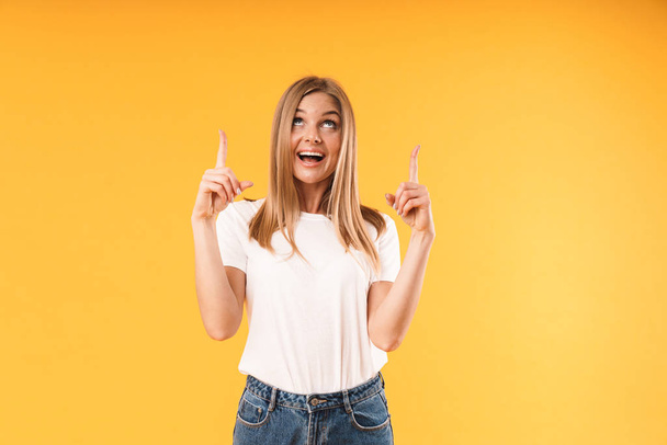 Image of cheerful blond woman wearing casual t-shirt smiling at camera and pointing fingers at copyspace - Фото, изображение