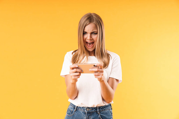 Image closeup of nervous young woman wearing casual t-shirt screaming while using smartphone - Photo, image