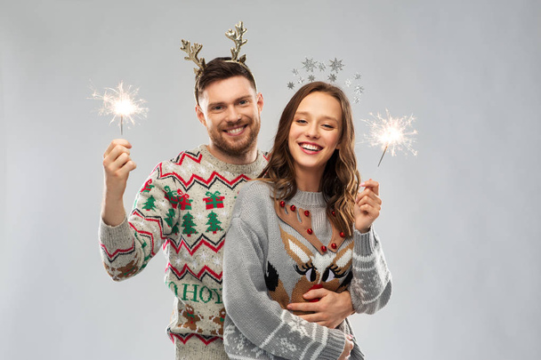 happy couple in christmas sweaters with sparklers - 写真・画像