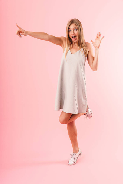 Full length image of happy blond woman expressing wonder and pointing finger at copyspace - Photo, Image