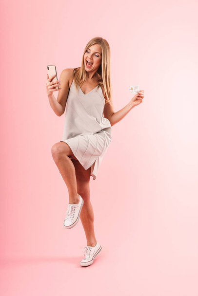 Image of excited blond woman smiling while holding credit card and smartphone - Foto, imagen