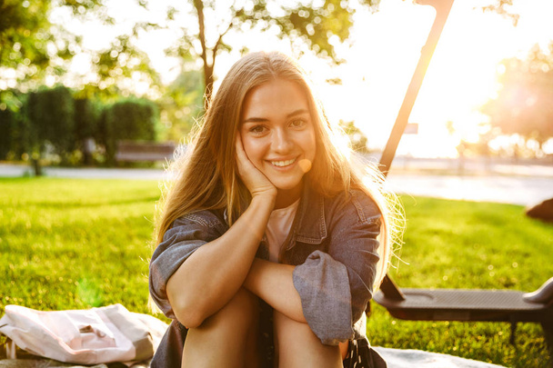 Cheerful smiling teenage girl sit on grass in nature green park. - Φωτογραφία, εικόνα