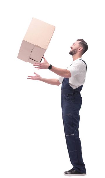 side view. smiling man in overalls catches a cardboard box - Φωτογραφία, εικόνα