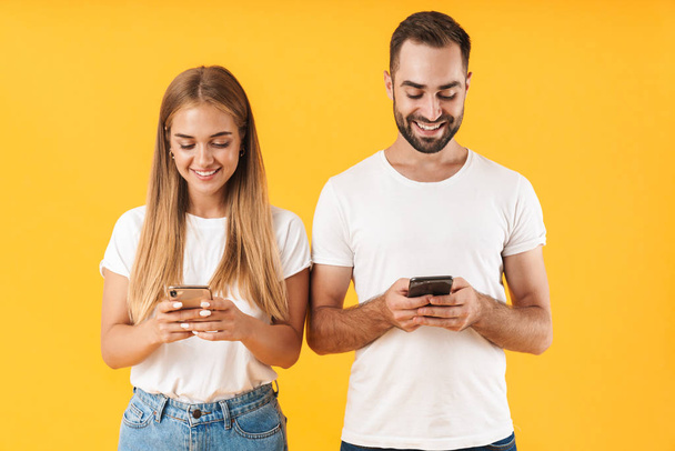 Image of positive couple ??smiling while using smartphones together - Фото, изображение