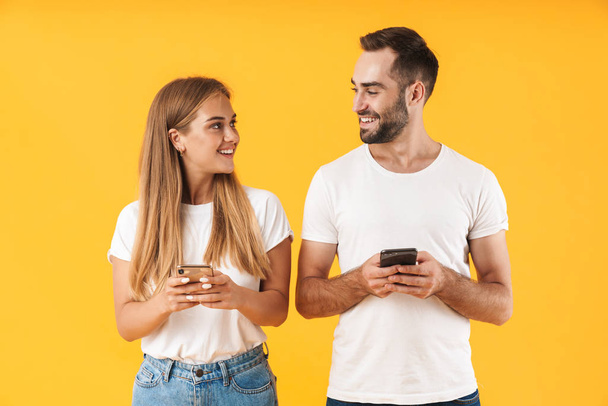 Image of beautiful couple smiling while using smartphones together - Φωτογραφία, εικόνα