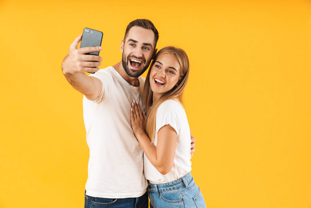 Image of joyful couple smiling while taking selfie photo on cellphone - Foto, afbeelding