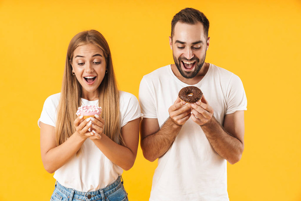 Image of joyful couple smiling while holding sweet donuts together - Foto, Bild