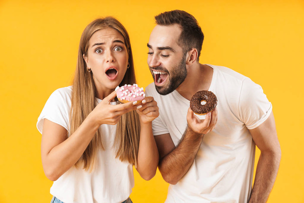 Image of happy couple smiling while eating sweet donuts together - Foto, imagen