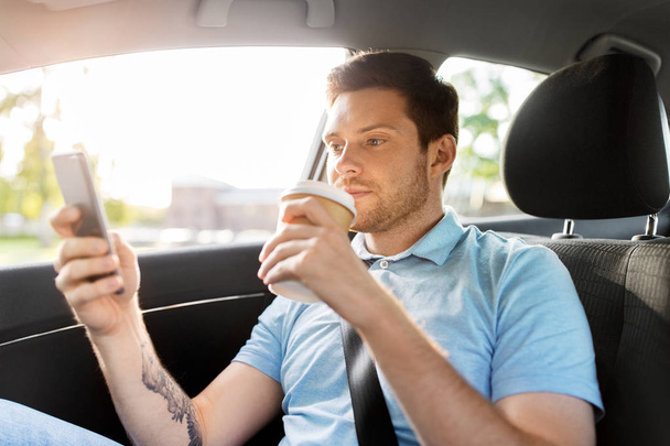 passenger drinking coffee using smartphone in car - Photo, Image
