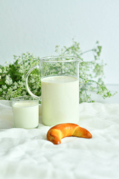 Glaskrug mit frischer Milch mit Glas und Croissant auf weißem Hintergrund. Milchkonzept - Foto, Bild