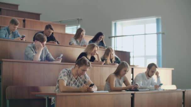 Een saaie lezing aan de Universiteit, studenten kijken naar de schermen van smartphones. Veel mensen - Video