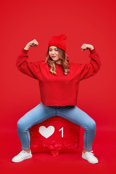 Confident strong woman in beanie sitting on like sign - Foto, Imagen