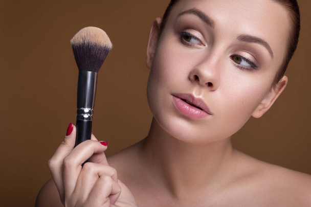 Caucasian brunette woman apply blush on a cheekbone with a brush - Fotó, kép