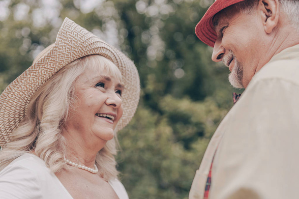 Portret starej kobiety, która szczęśliwie patrzy na dziadka z oczami i uśmiecha się do niego. Szczęśliwa para tańczy w parku i pamięta młodzież - Zdjęcie, obraz