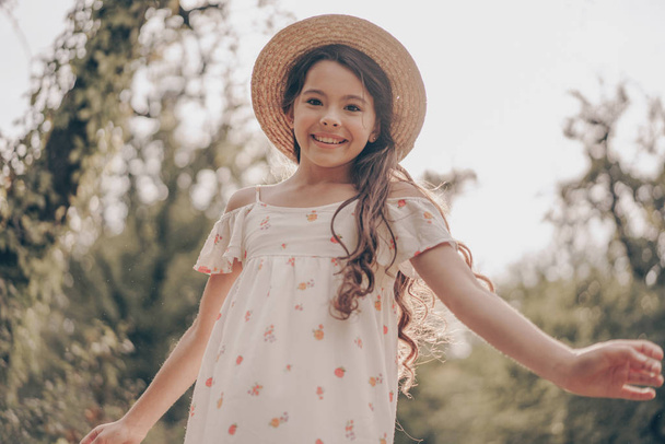Pretty young girl model on sunset in park wearing in sundress and hat. Portrait of beautiful child in park in summer - Foto, Imagem