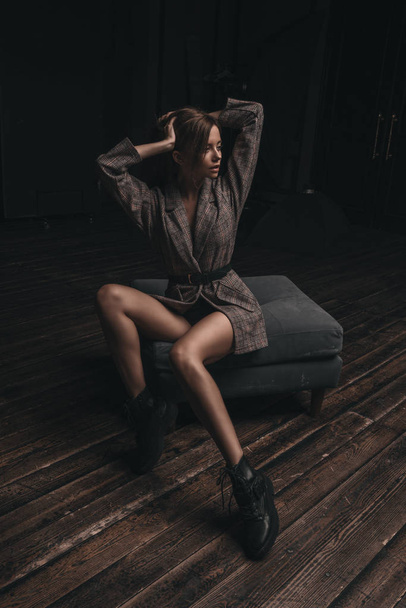 Mulher sexy quente em terno clássico e botas posando no estúdio loft em poltrona no fundo preto. sedutor glamour jovem modelo retrato
. - Foto, Imagem