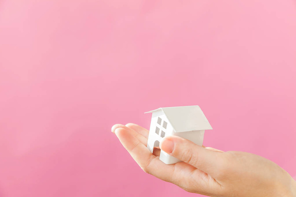 Simplemente diseñe la mano femenina de la mujer que sostiene la casa blanca miniatura del juguete aislada en el fondo de moda colorido pastel rosa
 - Foto, imagen