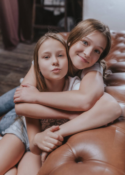 Two young pretty sisters portrait. Beautiful cheerful girls sitting on the bed at home - Photo, Image