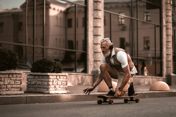 Adult bearded man portrait with longboard. Stylish model in casual clothes ride skateboard on city street background. Outdoors style. Sport lifestyle - Photo, Image